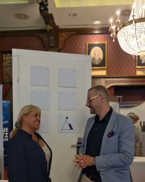 Andreas Meyer im Gespräch mit Claudia Conen vor einer Tür mit Bildern