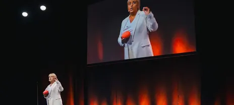 Claudia Conen auf einer großen Bühne, hinter ihr die Leinwand