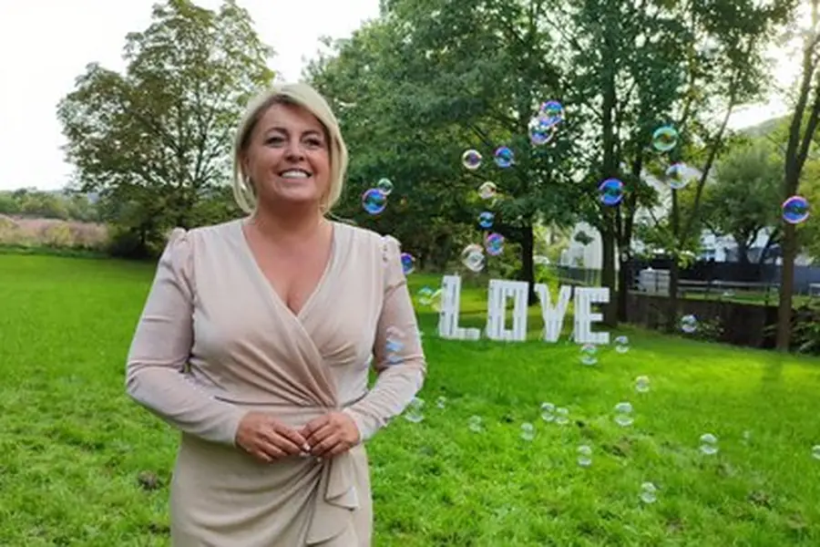 Claudia Conen im hellen Kleid auf einer Wiese, dahinter die Buchstaben LOVE und Seifenblasen