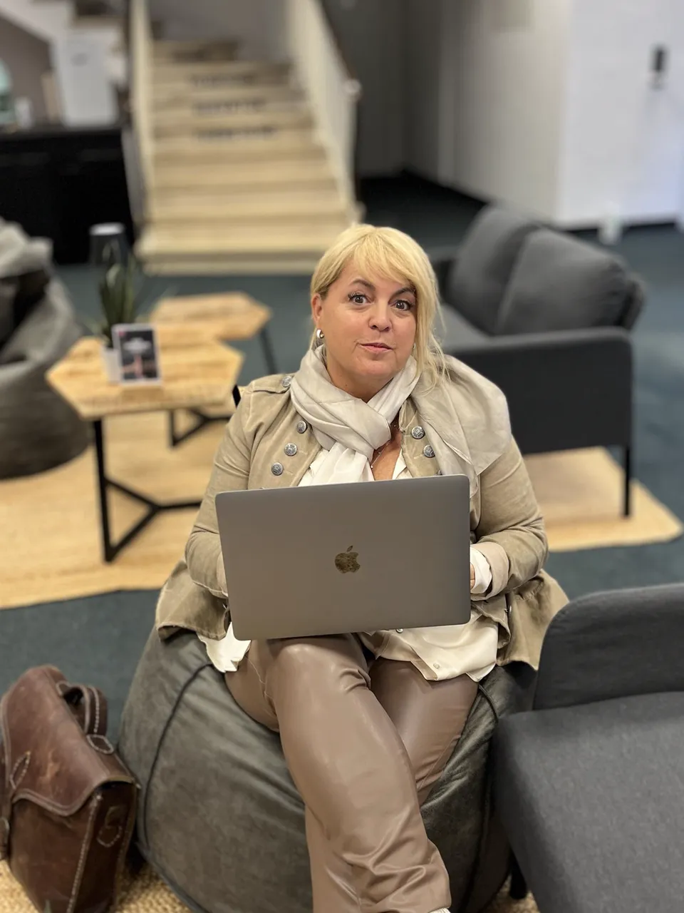 Claudia Conen mit Laptop in einer Lounge, den Blick zur Kamera